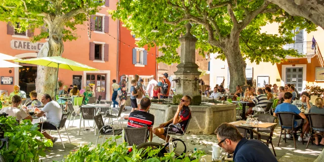 Place centrale du village de Villedieu avec des personnes qui se restaurent