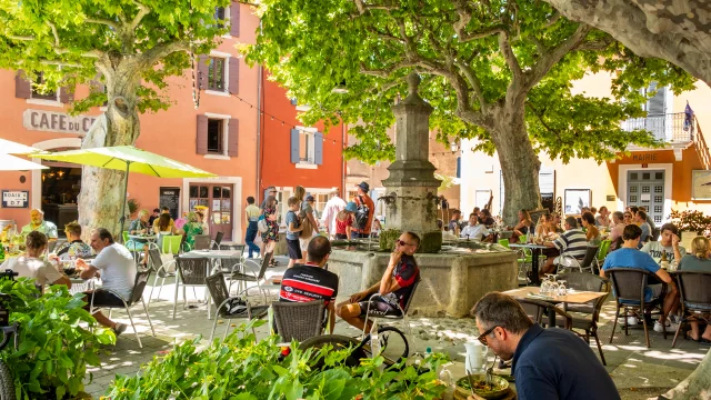 Place centrale du village de Villedieu avec des personnes qui se restaurent